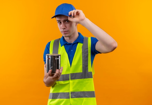 Молодой строитель в строительной форме и кепке держит контейнер с краской