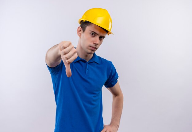 Young builder man wearing construction uniform and safety helmet doing angry thumbs down