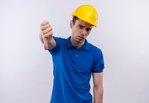 Young builder man wearing construction uniform and safety helmet doing angry thumbs down