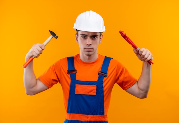 Young builder man wearing construction uniform and safety helmet holds a wrench and groove pliers