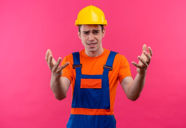 Молодой строитель человек в строительной форме и защитной каске возмущен