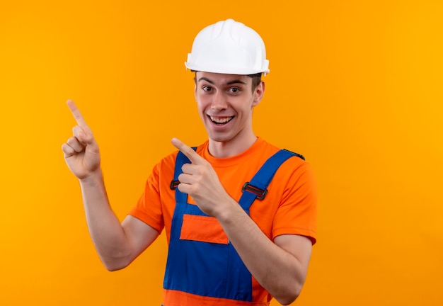 Young builder man wearing construction uniform and safety helmet, pointing up with fingers