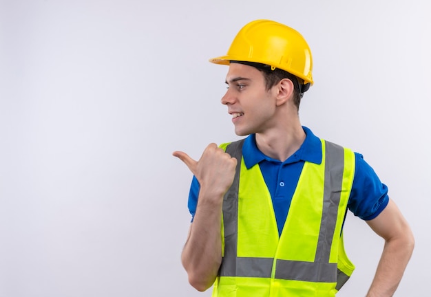 Il giovane costruttore che indossa l'uniforme da costruzione e il casco di sicurezza punta a destra con l'indice