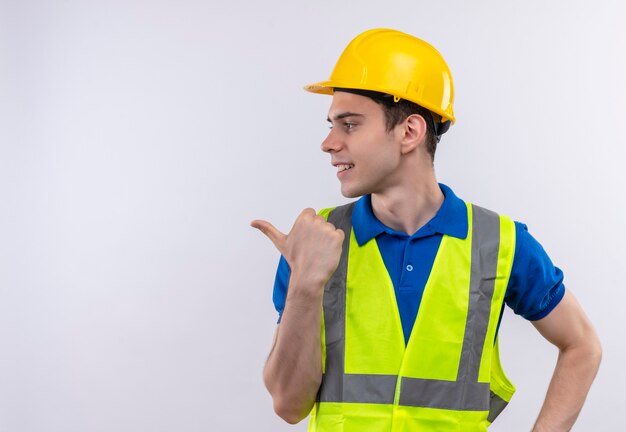 Молодой строитель в строительной форме и защитном шлеме указывает вправо указательным пальцем