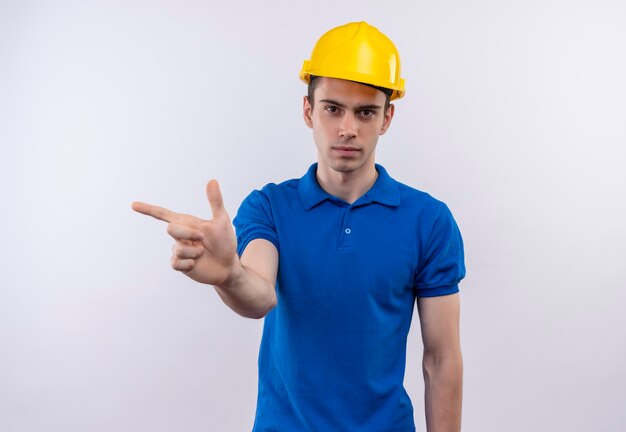 Young builder man wearing construction uniform and safety helmet points to the right with forefinger
