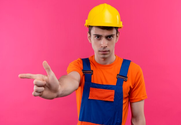 Young builder man wearing construction uniform and safety helmet points to the right