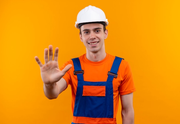 왼손으로 5를 보여주는 건설 유니폼과 안전 헬멧을 착용하는 젊은 작성기 남자
