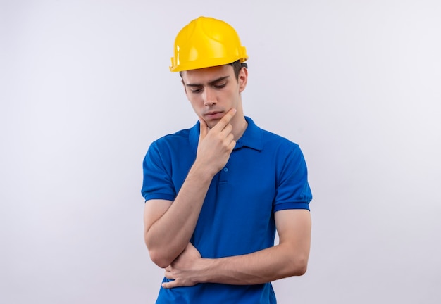 Uomo del giovane costruttore che indossa l'uniforme della costruzione e il pensiero del casco di sicurezza