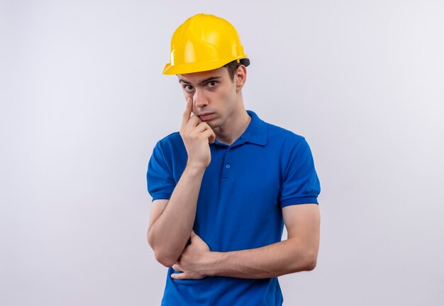 Young builder man wearing construction uniform and safety helmet thinking