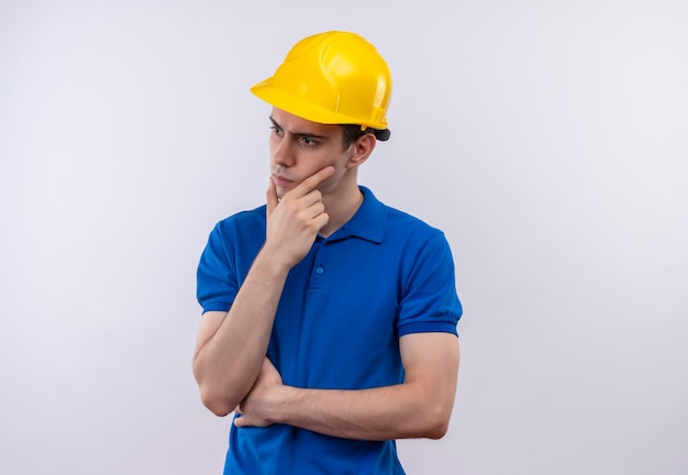 Uomo del giovane costruttore che indossa l'uniforme della costruzione e il pensiero del casco di sicurezza