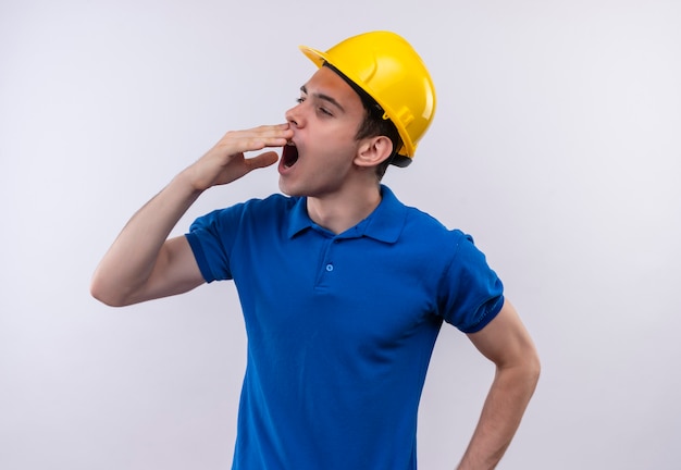 Young builder man wearing construction uniform and safety helmet yawns