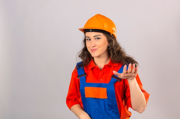 Young builder woman in construction uniform and safety helmet asking relax take easy raise hand hold calmness gesture smiling friendly over isolated white wall