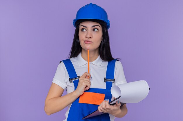 Young builder woman in construction uniform and safety helmet holding clipboard