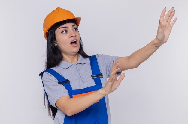 Young builder woman in construction uniform and safety helmet looking aside worried