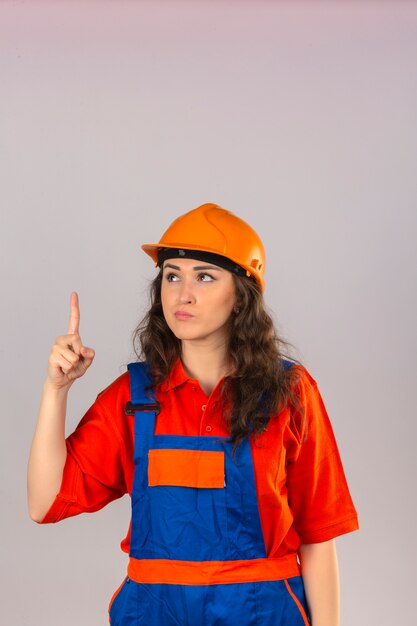 격리 된 흰 벽에 위험 경고 손가락으로 건설 유니폼과 안전 헬멧 서 젊은 작성기 여자