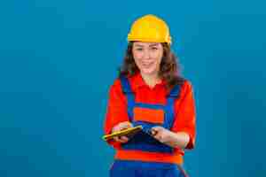 Free photo young builder woman in construction uniform and safety helmet standing with putty knife smiling friendly over isolated blue wall