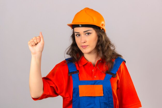 Young builder woman in construction uniform and safety helmet standing with raised fist winner concept over isolated white wall