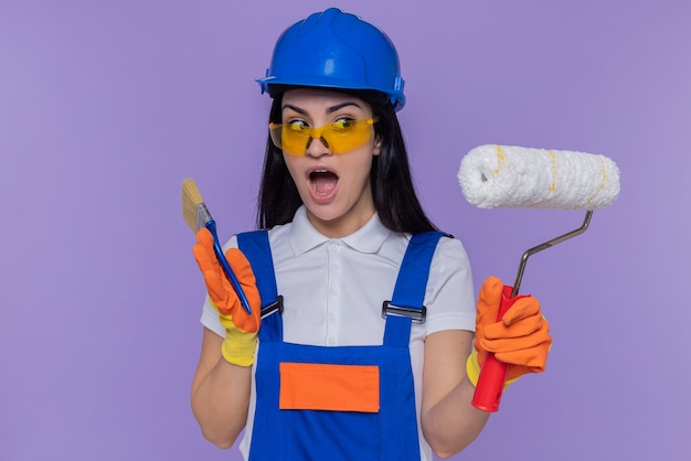 Young builder woman in construction uniform and safety helmet wearing rubber gloves