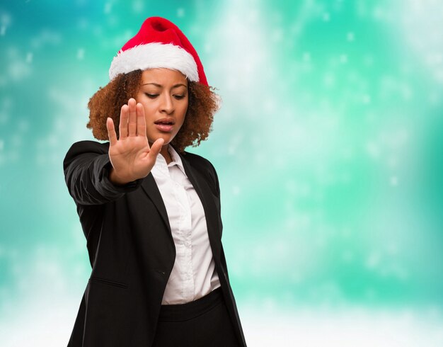 Young business black woman wearing a chirstmas santa hat putting hand in front