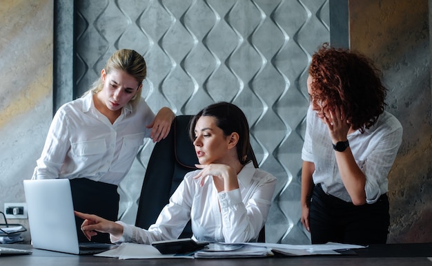 ラップトップコンピューターを使用してオフィスの机に座っている若いビジネス女性女性ディレクター作業プロセスビジネス会議を解決する同僚と協力してビジネス会議オフィス集団の概念