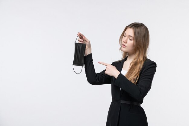 Young business lady in suit holding and pointing medical mask on isolated white wall