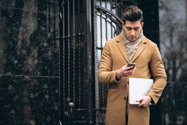 Young business man in coat with laptop outside