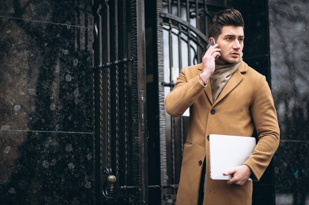 Молодой деловой человек в пальто с ноутбуком за пределами