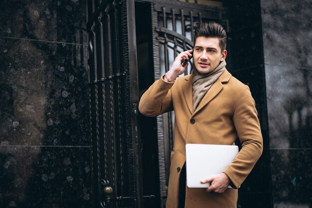 Young business man in coat with laptop outside