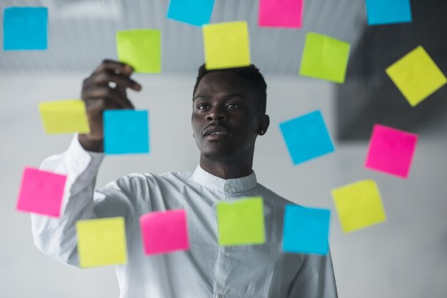 Young business man standing in front of stickers glass wall and write task on sticker at his office place