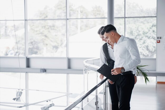 Young business people looking at documents and products standing at the office railing