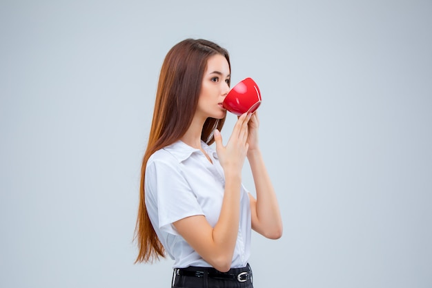 The young business woman i with red cup of coffee on a gray space