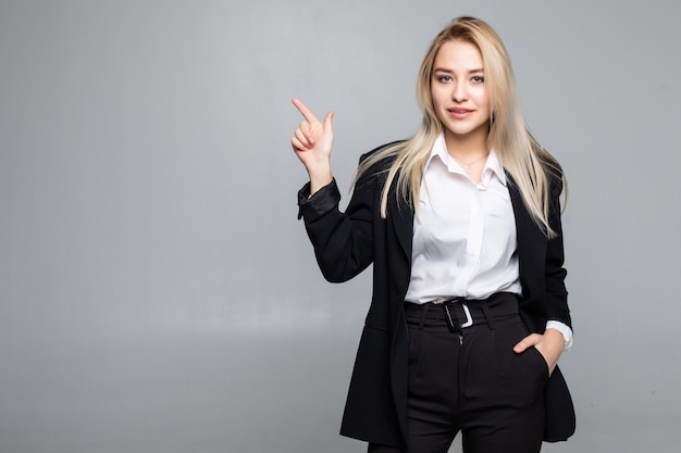Young business woman pointing finger to the side on isolated grey wall