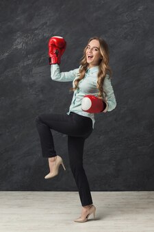 Young business woman in red boxing gloves smiling to camera. ready to fight in corporate battle, business competition and perseverance concept, black studio background