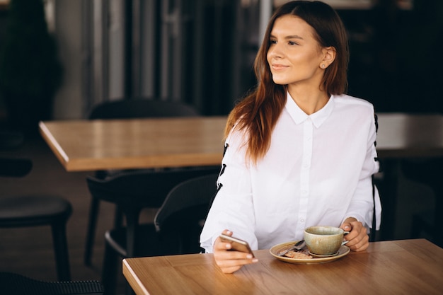 コーヒーと電話でカフェに座っている若いビジネスの女性