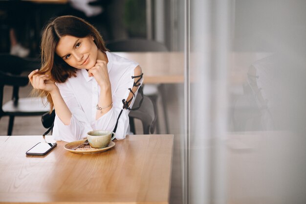 コーヒーと電話でカフェに座っている若いビジネスの女性