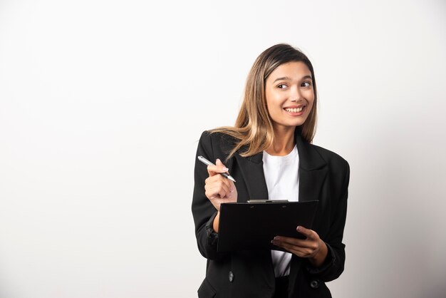 Young business woman standing with her clipboard on white wall. 