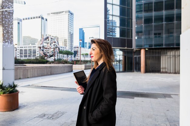 Free photo young business woman standing with tablet outside