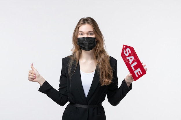 Молодая деловая женщина в костюме, одетая в медицинскую маску и показывающая продажу, делая жест на изолированной белой стене