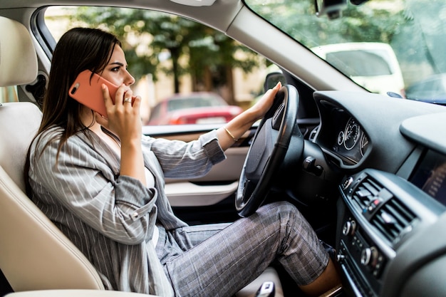 Free photo young business woman using her phone while driving the car