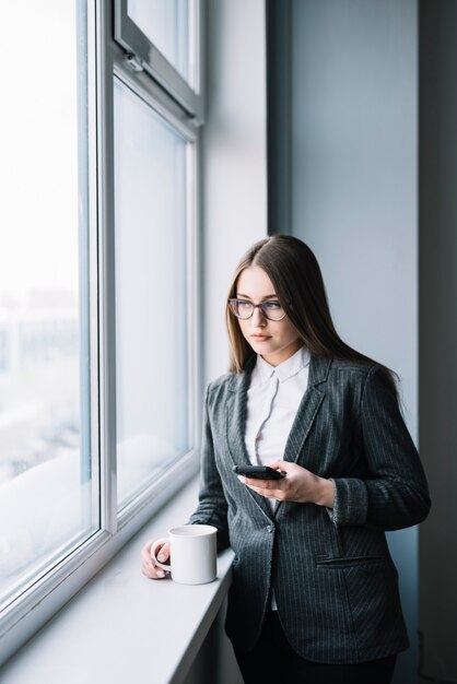 Free photo young business woman using smartphone at window