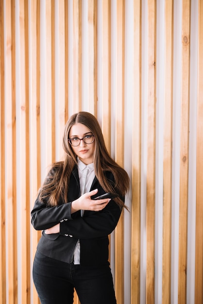 Young business woman using smartphone at wooden wall