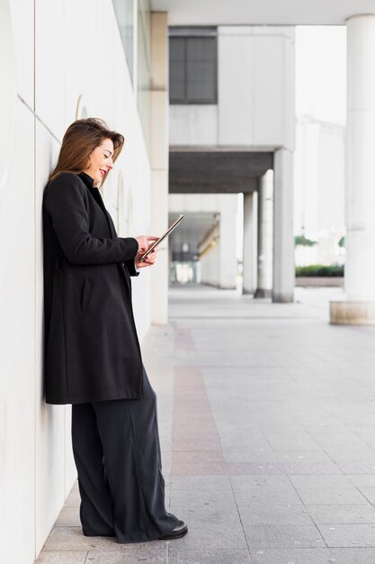 外の壁にもたれてタブレットを使用して若いビジネス女性