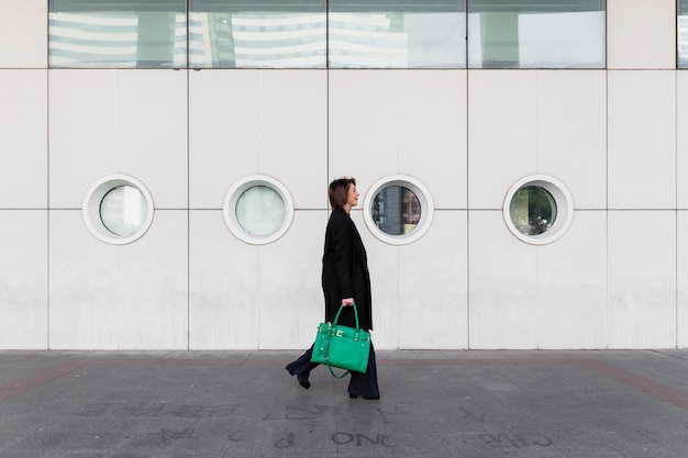 Foto gratuita giovane donna di affari che cammina in strada con la borsa verde