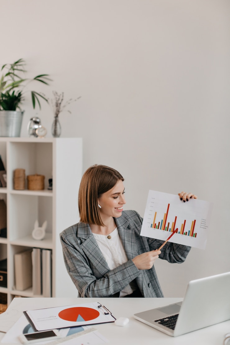 Free Photo young business woman in white office with smile shows graphic, talking to customers on skype.