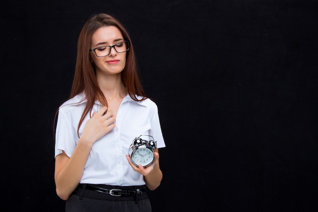 The young business woman with alarm clock on black wall
