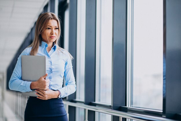 オフィスで立っているラップトップを持つ若いビジネス女性