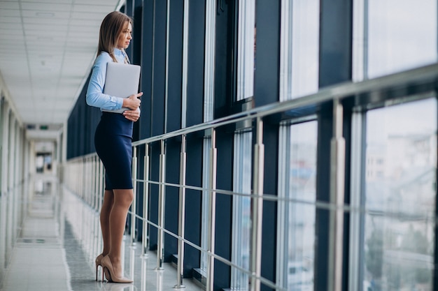 オフィスで立っているラップトップを持つ若いビジネス女性