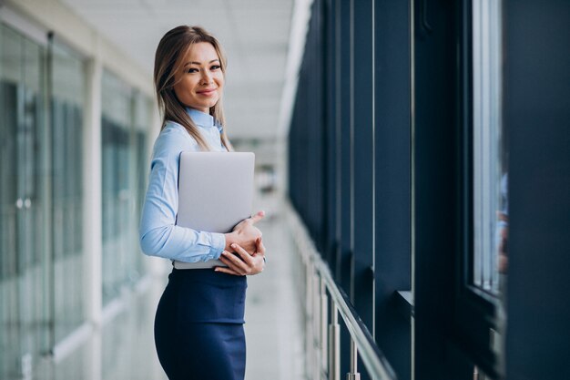 オフィスで立っているラップトップを持つ若いビジネス女性