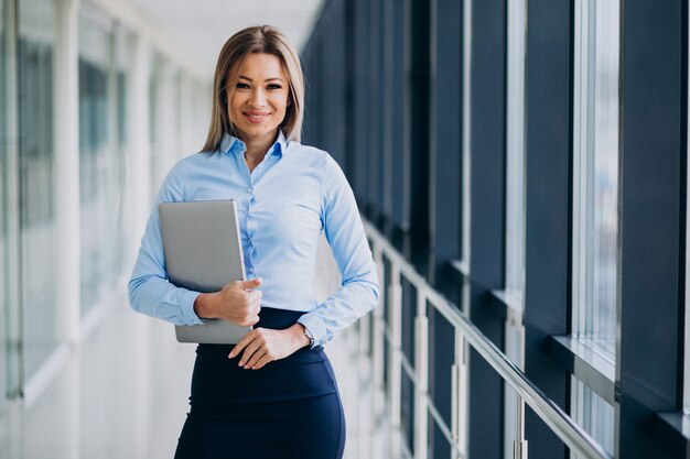 オフィスで立っているラップトップを持つ若いビジネス女性