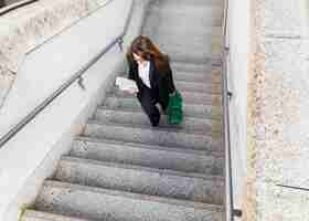 Free photo young business woman with newspaper and bag walking up stairs